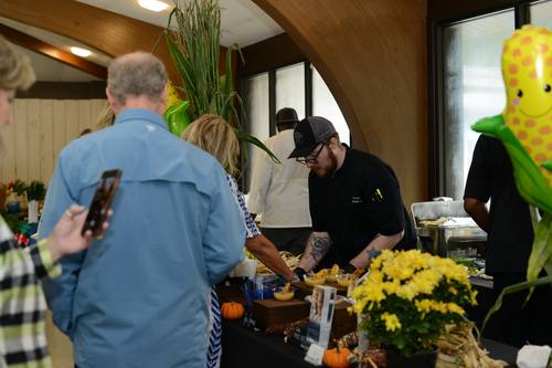 Chef with tattoos serving a smiling guest a plated bite