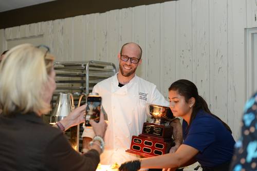 Chef receiving the trophy from a teammate in the kitchen