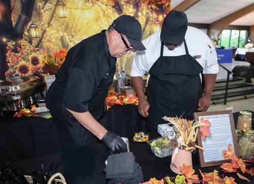 Two chefs lean in to inspect dishes at a fall-themed station