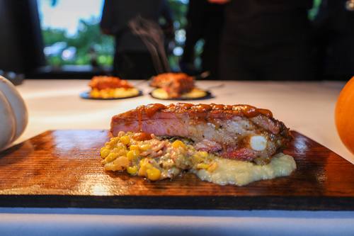 Glazed pork rib plated with charred corn and creamy grits